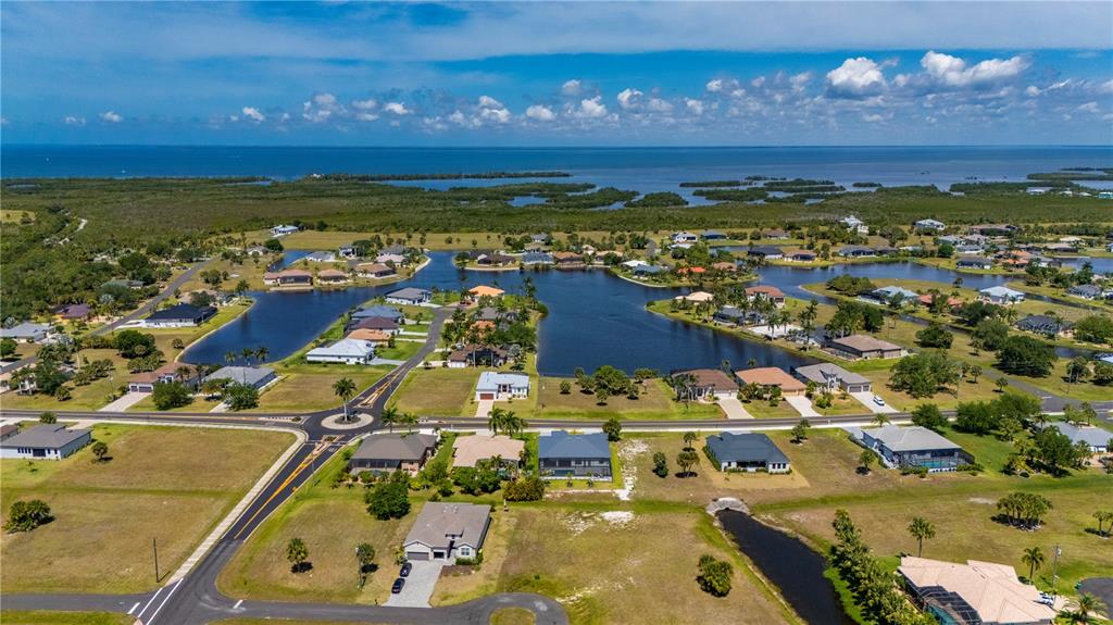 An aerial view shows a residential neighborhood with houses surrounding a large lake near water — 16429 AYSON WAY, PUNTA GORDA, FL