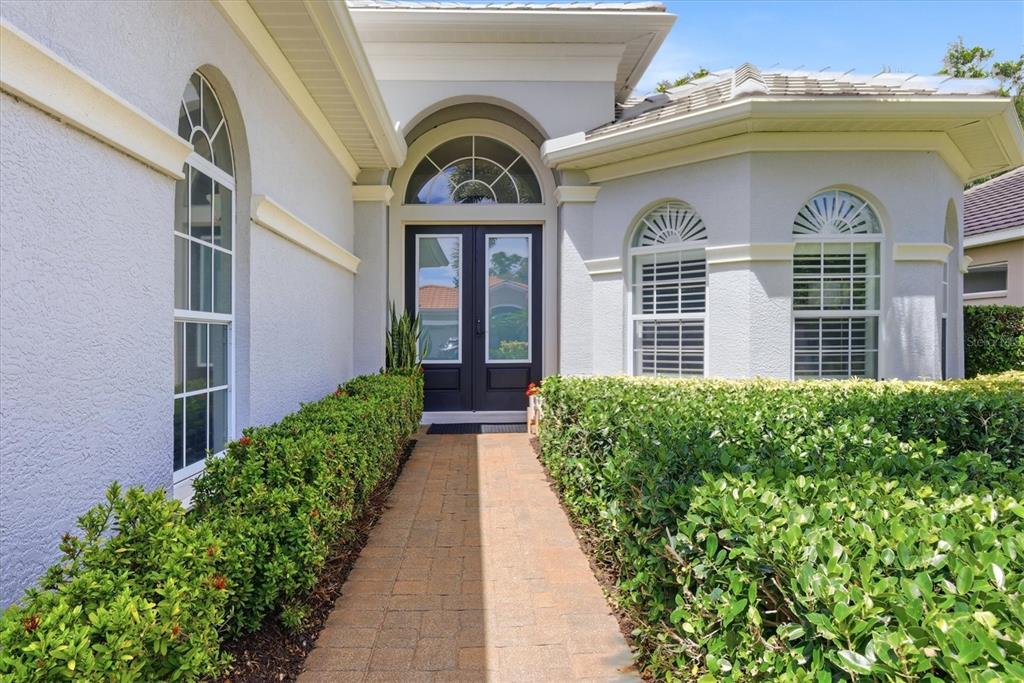 A brick walkway leads to the dark double front doors of a light-colored stucco house — 12323 THORNHILL COURT, LAKEWOOD RANCH, FL