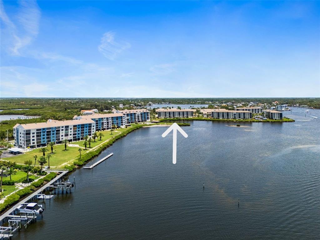 An aerial view shows waterfront apartment buildings with a white arrow pointing to a structure — 8251 BRENT STREET UNIT 936, PORT RICHEY, FL