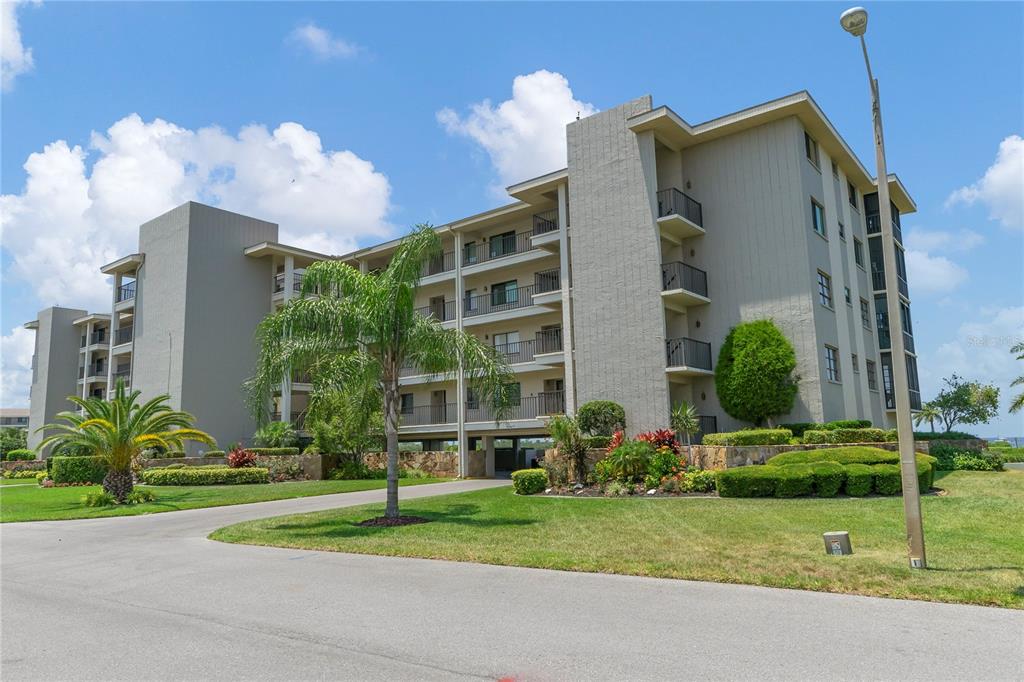 A multi-story apartment building with balconies and palm trees sits on a landscaped lawn — 8251 BRENT STREET UNIT 936, PORT RICHEY, FL
