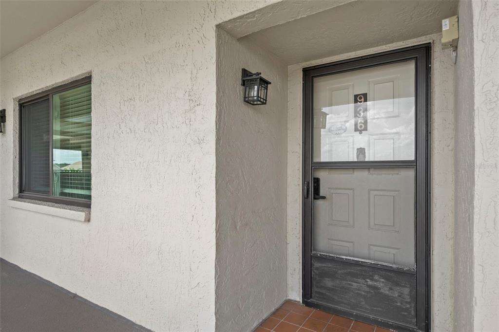 A beige stucco exterior wall features a front door with a storm door and window — 8251 BRENT STREET UNIT 936, PORT RICHEY, FL