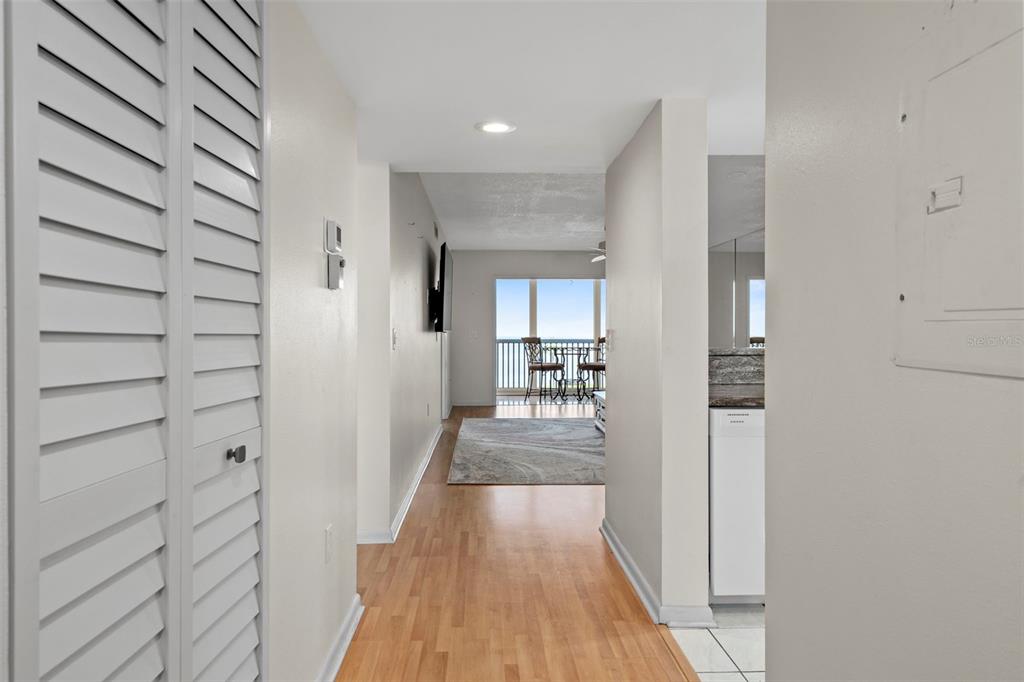 A hallway with light wood flooring leads to a living area with a balcony view — 8251 BRENT STREET UNIT 936, PORT RICHEY, FL