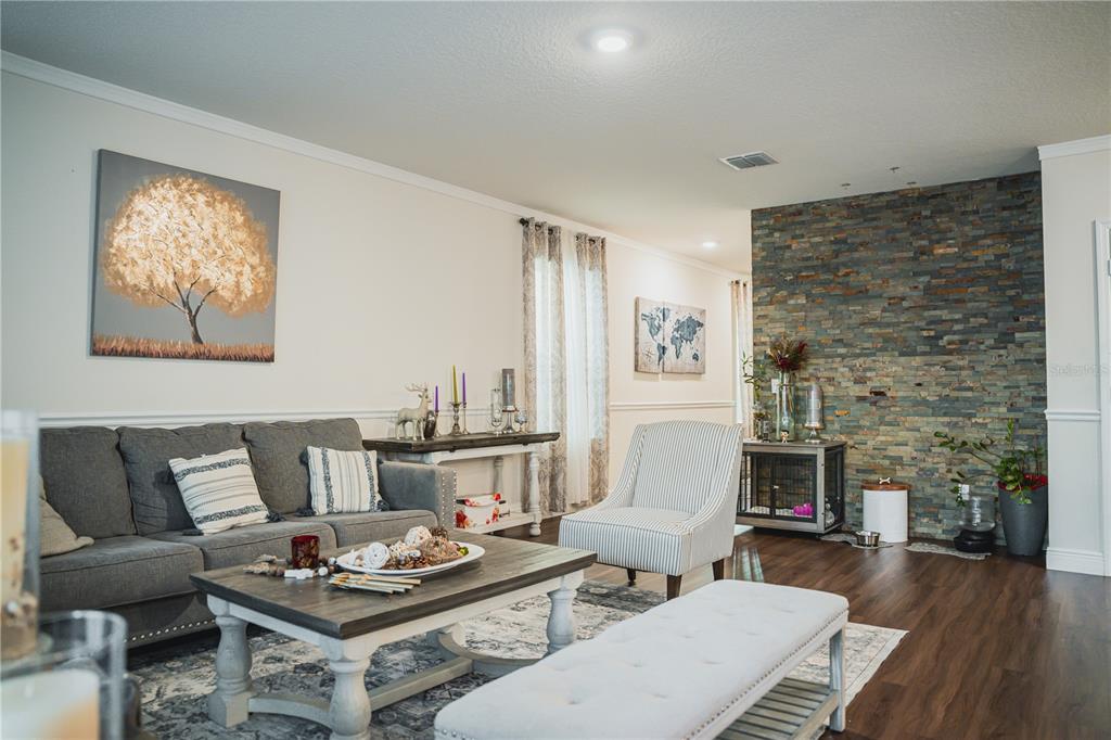 A living room features a grey sofa, a stone accent wall, and wood-look flooring — 2907 SUMMER GREEN TRAIL, KISSIMMEE, FL