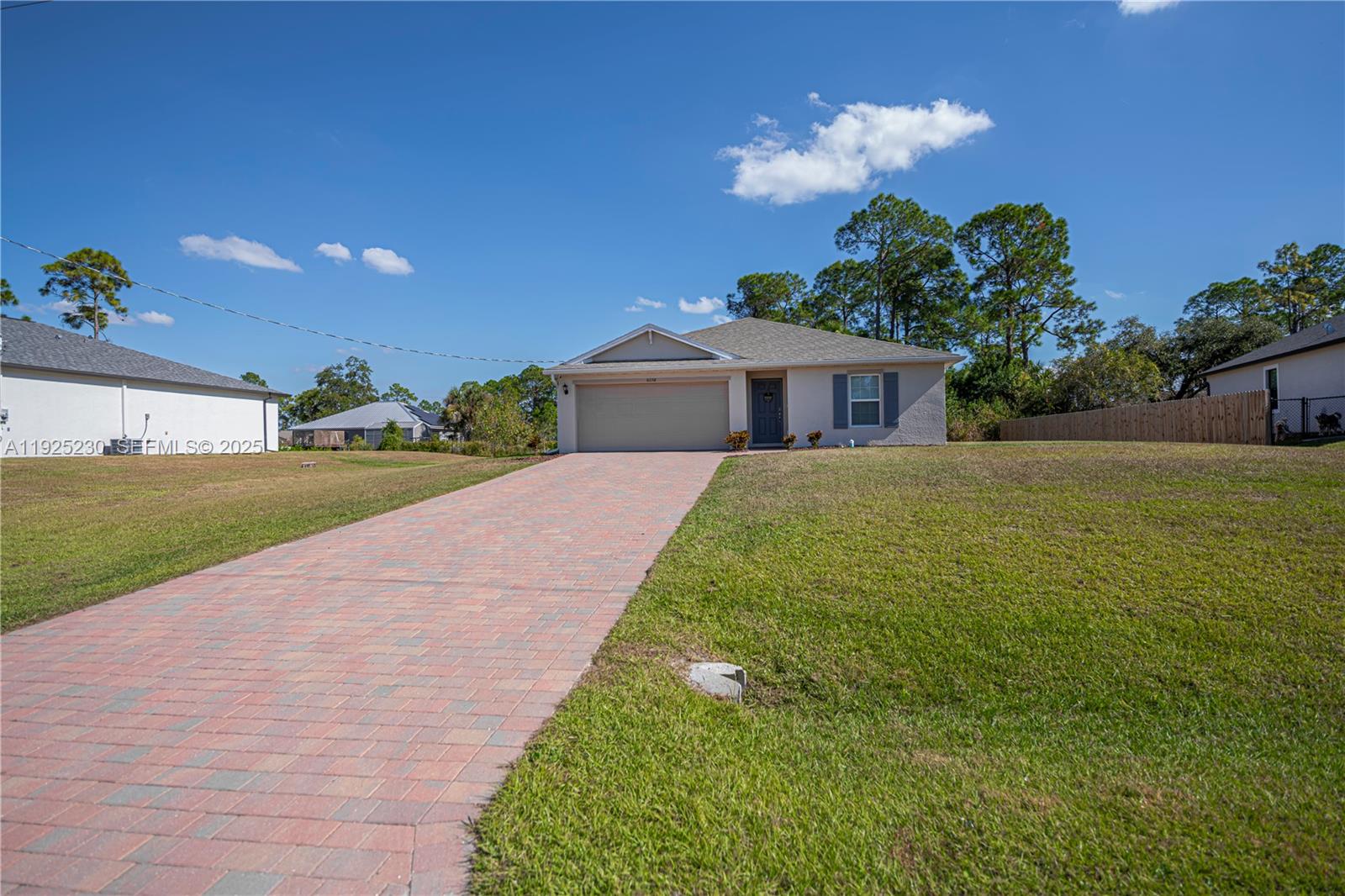 A single-story house with a paved driveway and a large front lawn under a blue sky — 6058 S Moss Circle, La Belle FL 33935, LA BELLE, FL