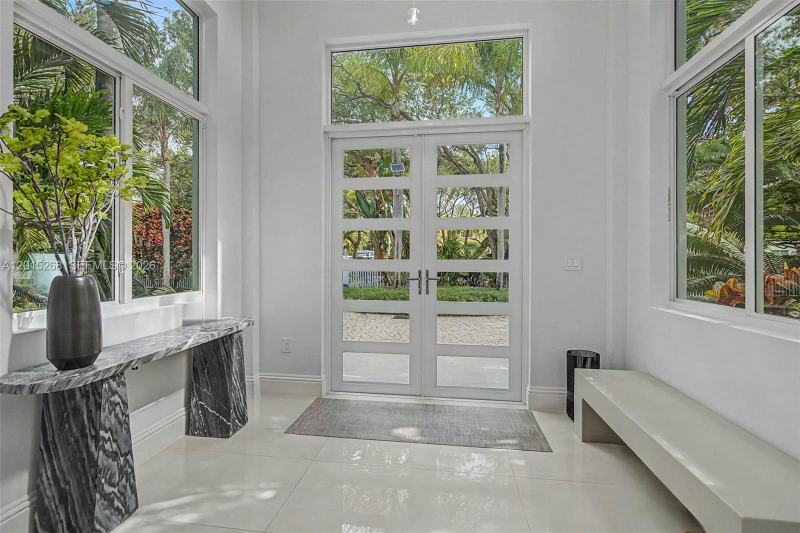 A bright entryway features white walls, tile floors, a marble console table, and double doors — 5790 SW 96th St, Pinecrest FL 33156, PINECREST, FL
