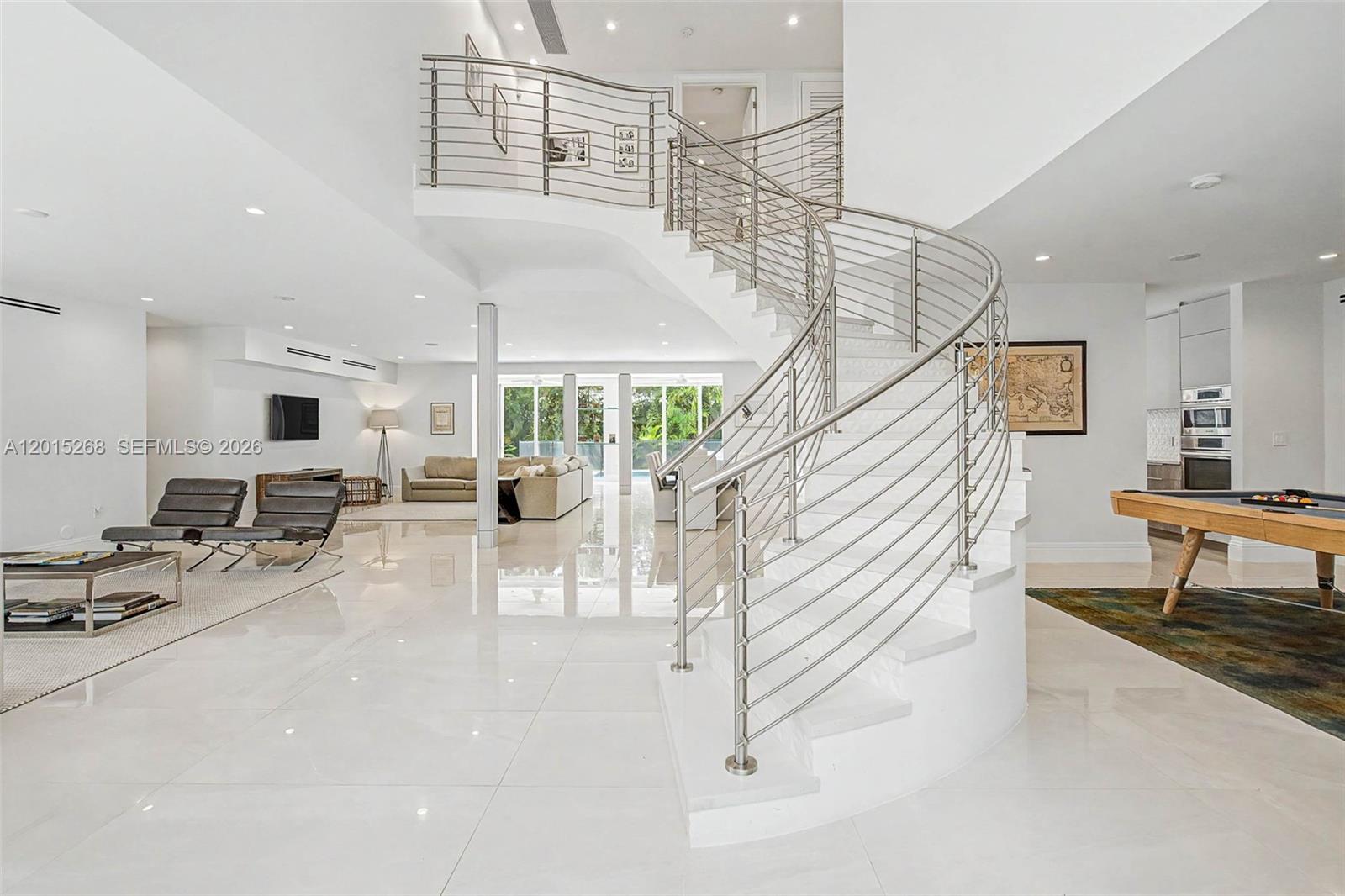 A spacious, modern living area features a prominent curved staircase with a metal railing — 5790 SW 96th St, Pinecrest FL 33156, PINECREST, FL