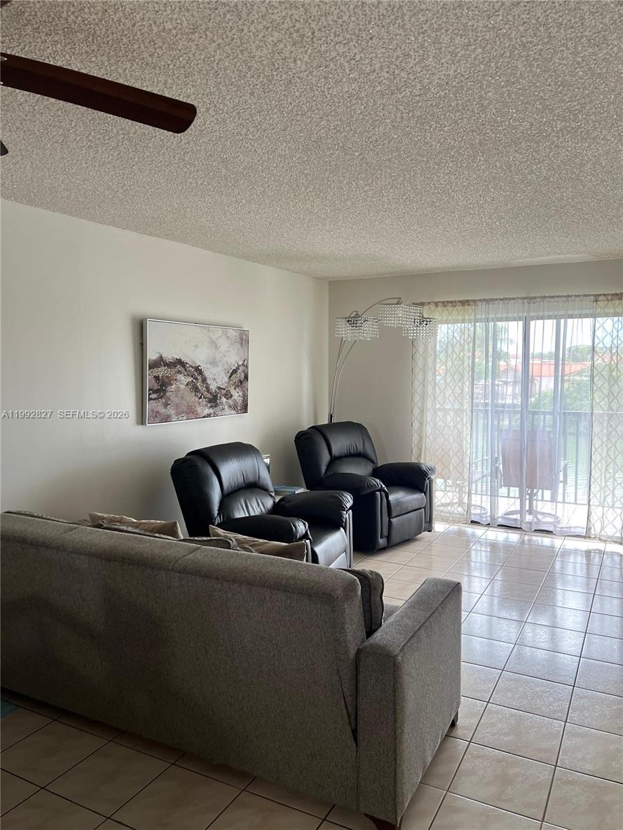 A living room features a gray sofa, two black recliners, tile flooring, and a balcony view — 6465 W 27th Ave # 202, Hialeah FL 33016, HIALEAH, FL