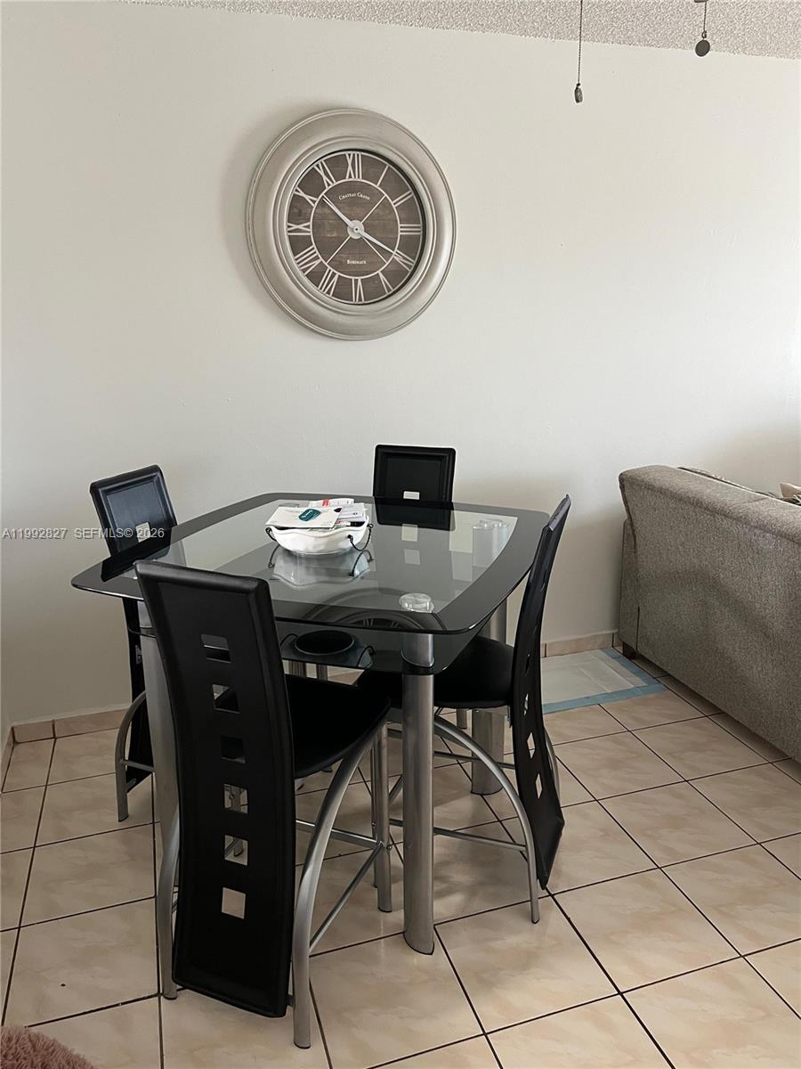 A dining area features a glass-topped table with four black chairs and a wall clock — 6465 W 27th Ave # 202, Hialeah FL 33016, HIALEAH, FL