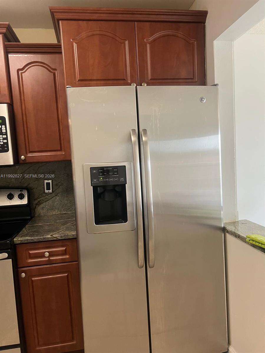 A stainless steel side-by-side refrigerator is positioned next to wooden kitchen cabinets and a stove — 6465 W 27th Ave # 202, Hialeah FL 33016, HIALEAH, FL