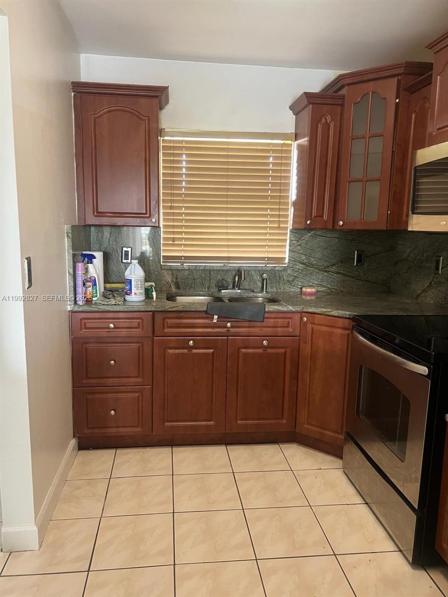 A kitchen features wood cabinets, a green stone backsplash, and light-colored tile flooring — 6465 W 27th Ave # 202, Hialeah FL 33016, HIALEAH, FL