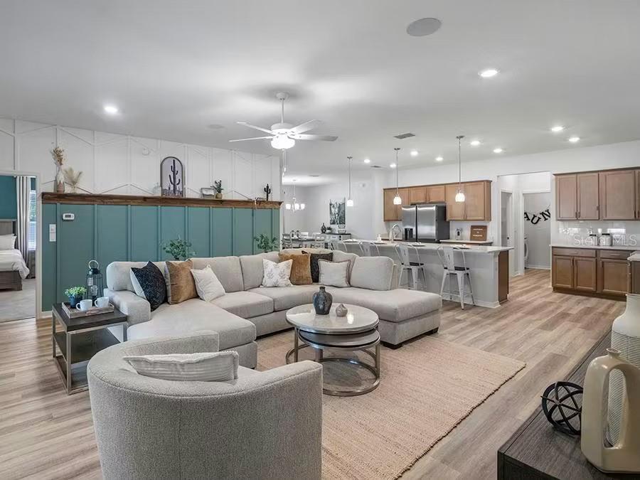 An open-concept living room and kitchen featuring a teal accent wall and sectional sofa — 8673 WILDFLOWER FIELD LANE, WILDWOOD, FL