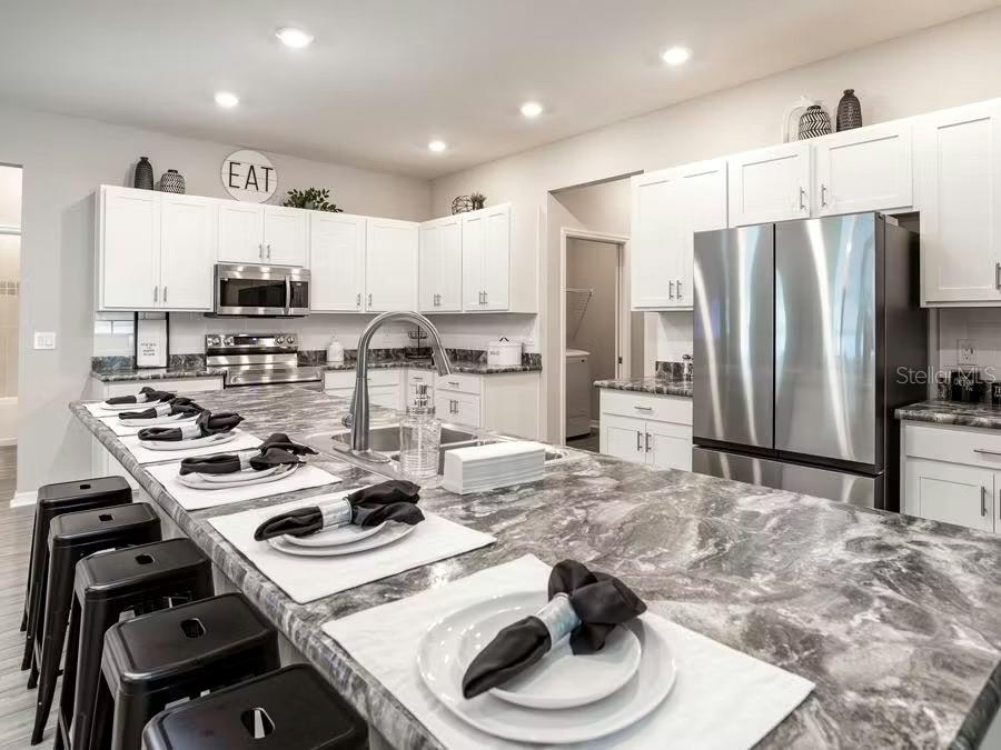 A kitchen features white cabinets, a large gray marble island, and stainless steel appliances — 8673 WILDFLOWER FIELD LANE, WILDWOOD, FL