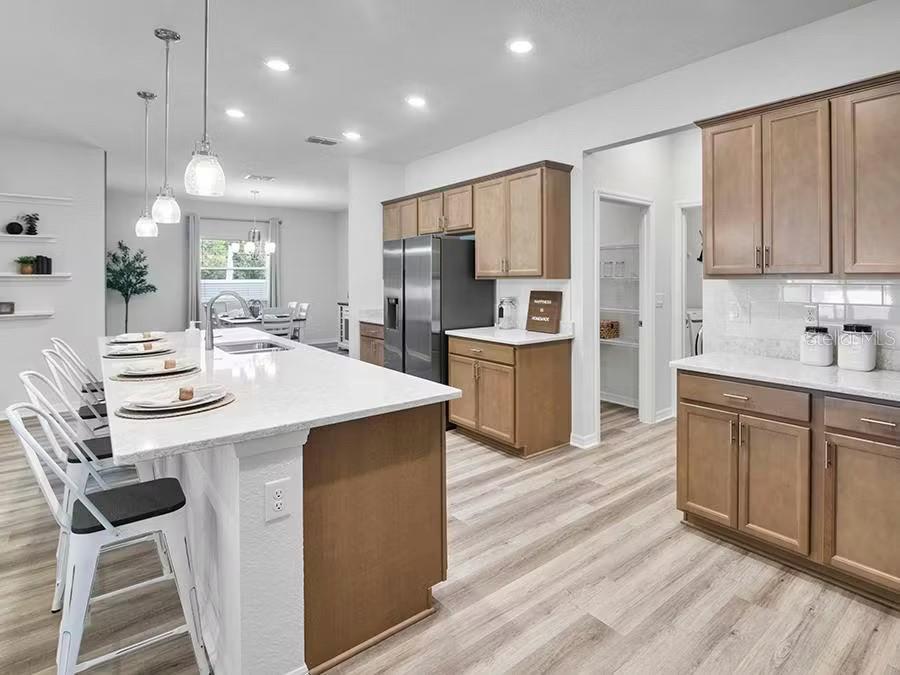 A modern kitchen features light wood cabinets, a large white island, and stainless steel appliances — 8673 WILDFLOWER FIELD LANE, WILDWOOD, FL