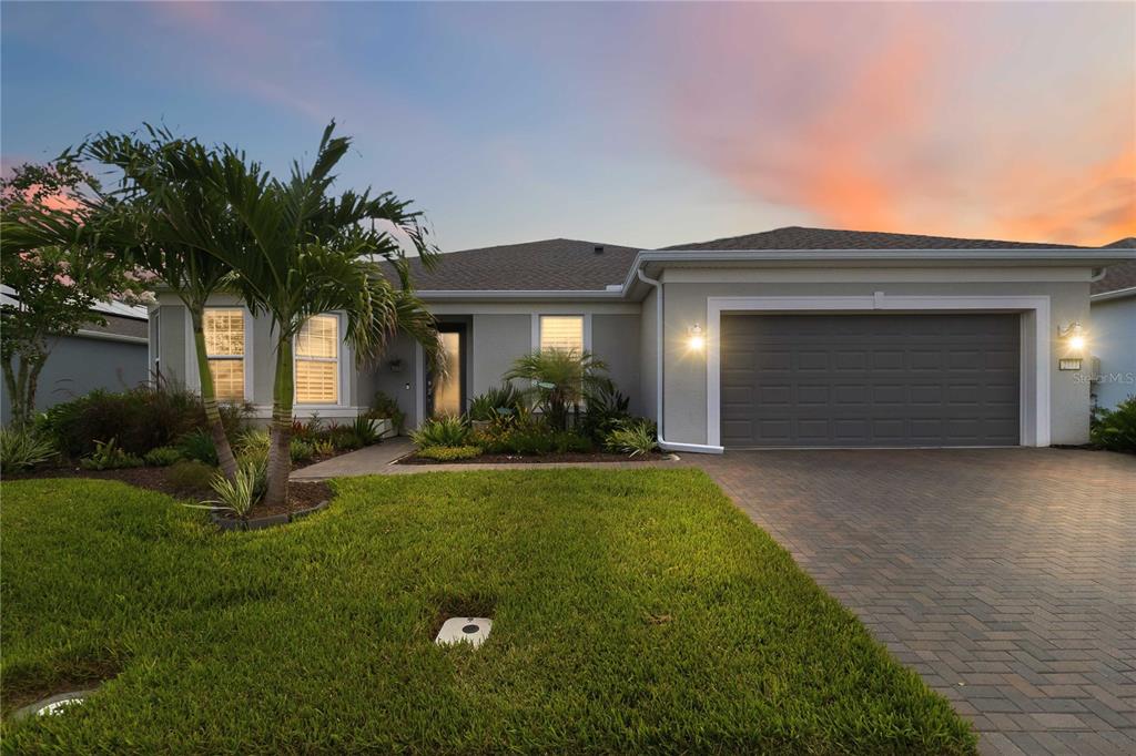 A single-story house with a gray garage, paved driveway, and palm tree at sunset — 2777 CHERRY BLOSSOM LOOP, ST CLOUD, FL