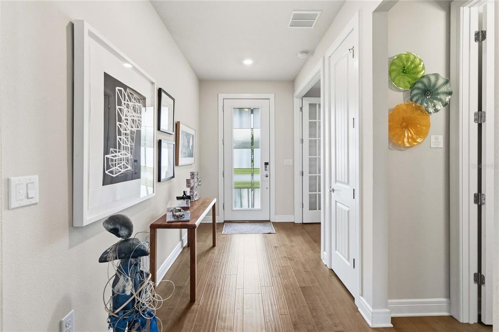 A bright entryway features hardwood floors, a glass-paneled front door, and wall-mounted art and decor — 2777 CHERRY BLOSSOM LOOP, ST CLOUD, FL