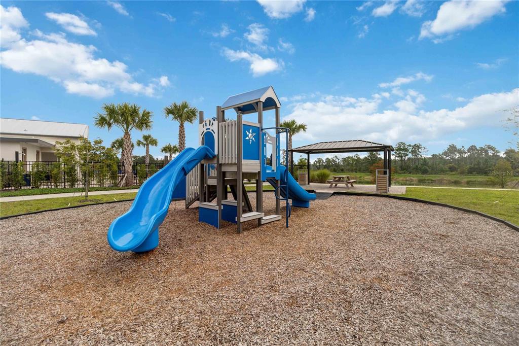 A playground with a blue slide structure sits on wood chips near a covered pavilion — 299 NINE IRON DRIVE, DAVENPORT, FL