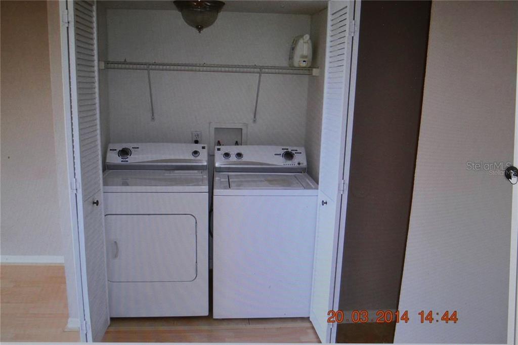 A laundry closet contains a white washer and dryer beneath a wire shelf — 13735 JUNIPER BLOSSOM DRIVE, TAMPA, FL