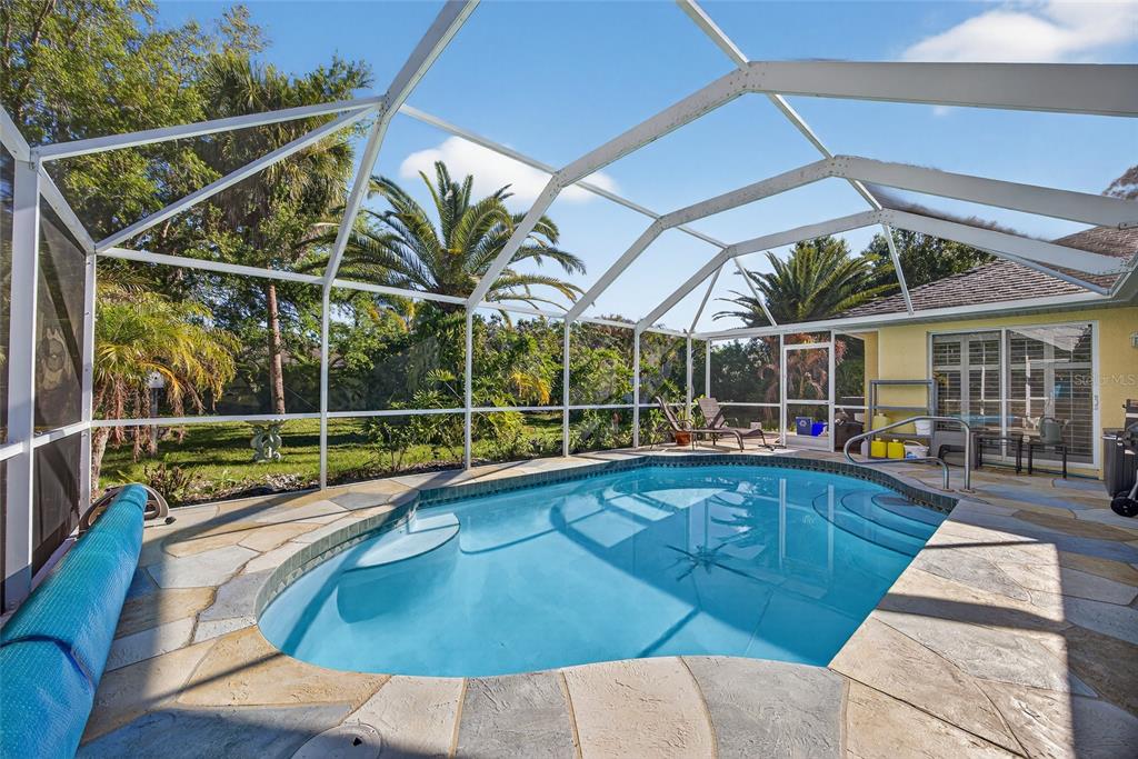 A screened-in swimming pool with stone decking sits in a backyard with palm trees — 7270 PARAGON ROAD, NORTH PORT, FL