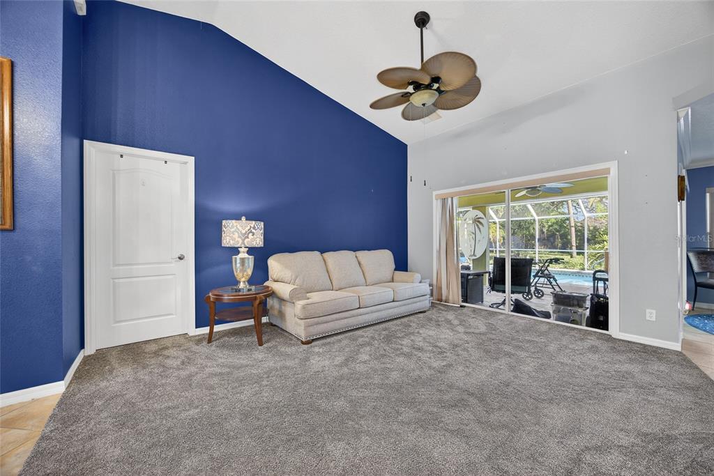A living room features a blue accent wall, beige sofa, gray carpet, and sliding glass doors — 7270 PARAGON ROAD, NORTH PORT, FL