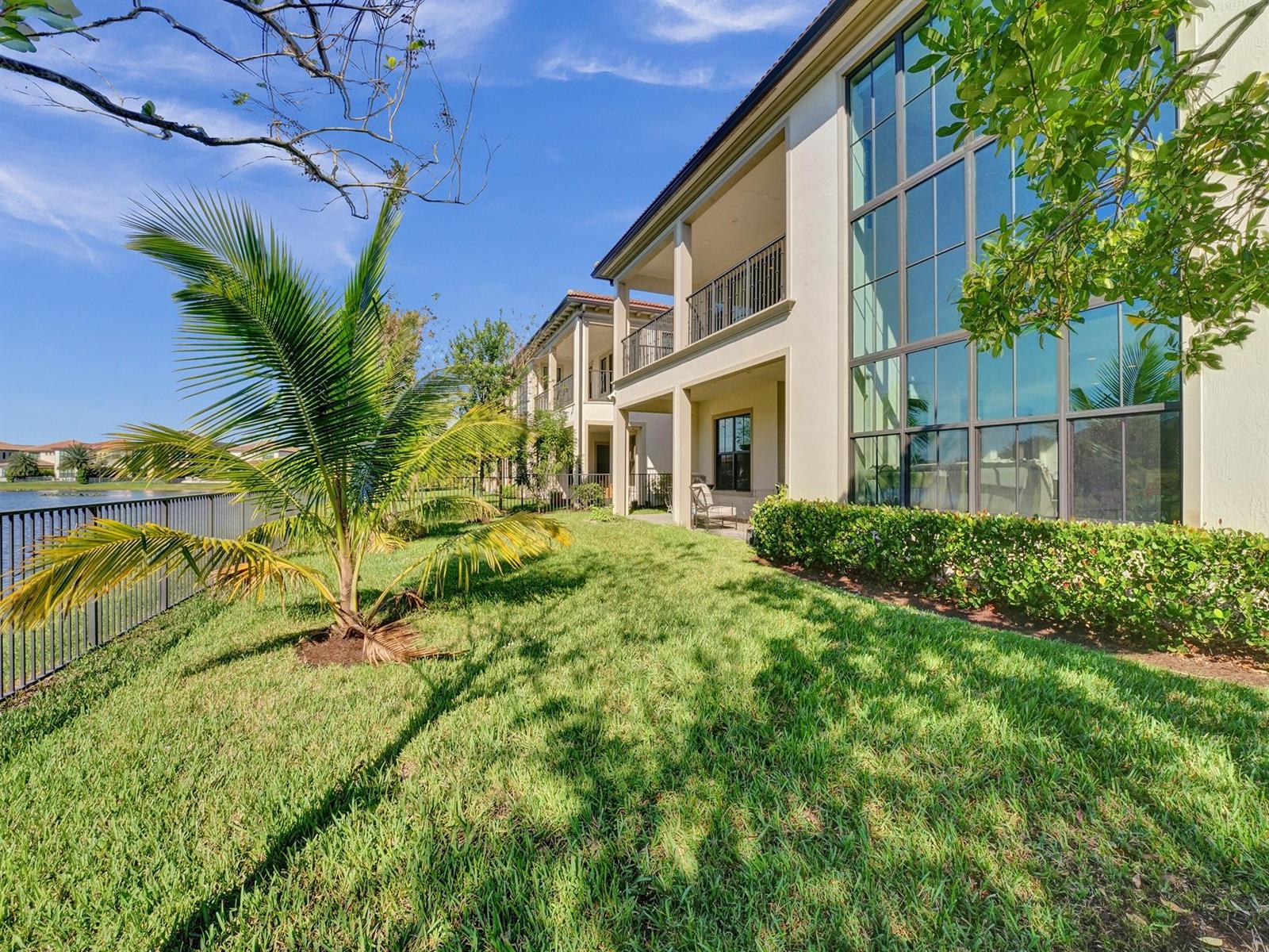 A multi-story building with large windows and balconies overlooks a grassy lawn and a lake — 9345 Carrington Avenue, Parkland FL 33076, PARKLAND, FL