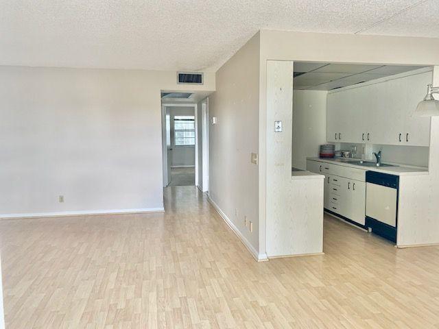 An interior view shows a living area with light wood flooring leading to a kitchen — 3063 Ainslie D, Boca Raton FL 33434, BOCA RATON, FL