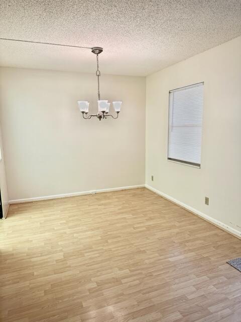 An empty dining room features light wood-look flooring, beige walls, and a hanging chandelier — 3063 Ainslie D, Boca Raton FL 33434, BOCA RATON, FL