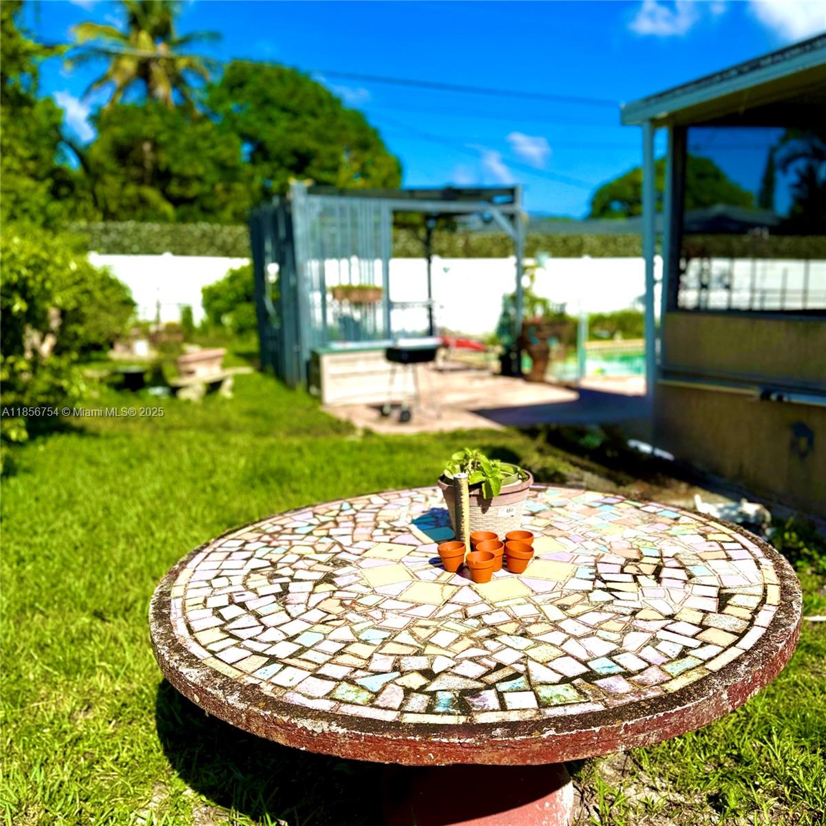 A mosaic-tiled round table sits in a grassy backyard with a patio and pergola — 17001 NE 6th Ct, North Miami Beach FL 33162, NORTH MIAMI BEACH, FL