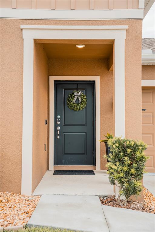 A dark front door with a wreath is set within a tan stucco entryway — 2326 BURNEY FALLS LANE, DAVENPORT, FL