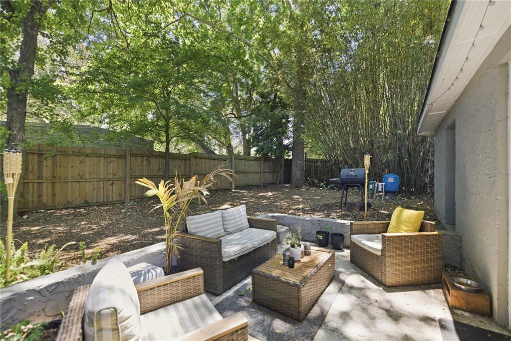 A patio with wicker furniture sits in a backyard with a wooden fence and trees — 3017 NE 24TH COURT, OCALA, FL