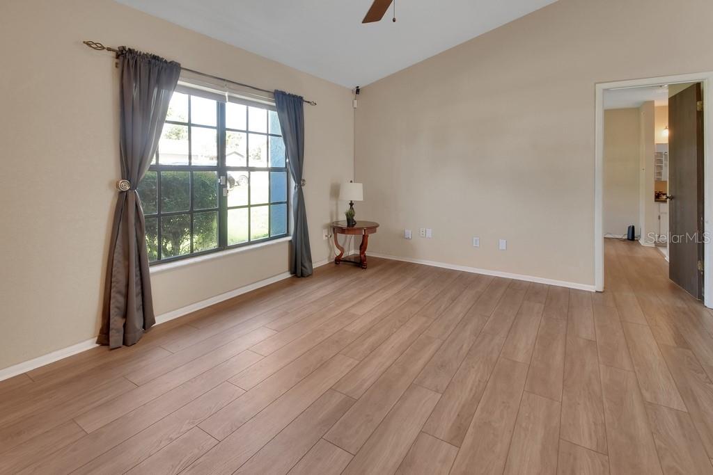 An empty room features light wood-look flooring, beige walls, a window with curtains, and a doorway — 3018 BONKIRK DRIVE, DELTONA, FL