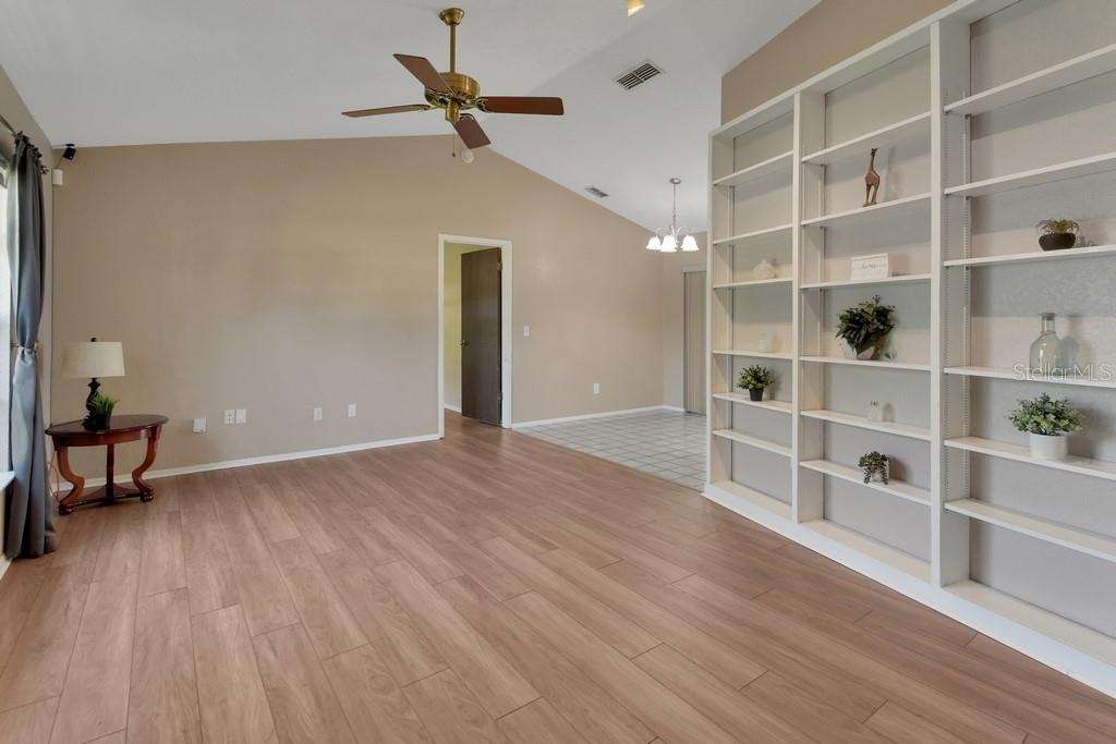 A living room features light wood-look flooring, a vaulted ceiling with a fan, and built-in shelving — 3018 BONKIRK DRIVE, DELTONA, FL