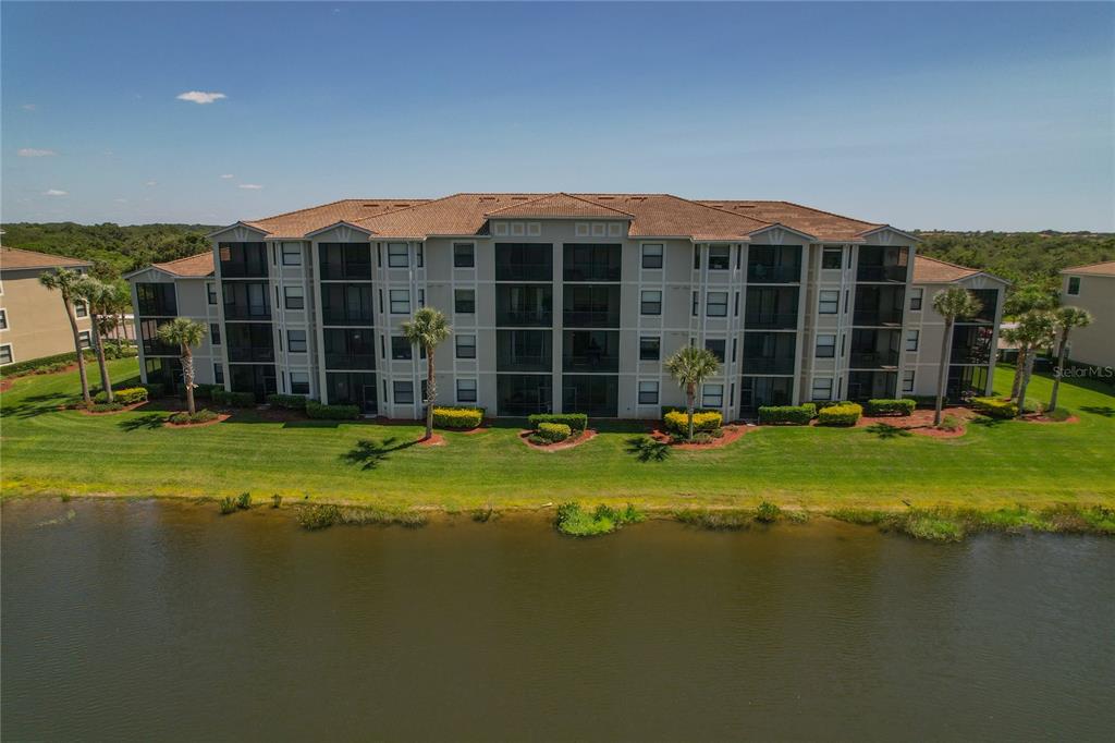 An aerial view of a multi-story apartment building situated next to a lake — 7015 RIVER HAMMOCK DRIVE UNIT 208, BRADENTON, FL