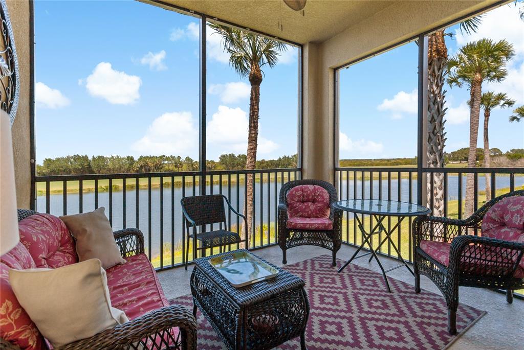 A screened-in patio features wicker furniture, a patterned rug, and views of a lake — 7015 RIVER HAMMOCK DRIVE UNIT 208, BRADENTON, FL