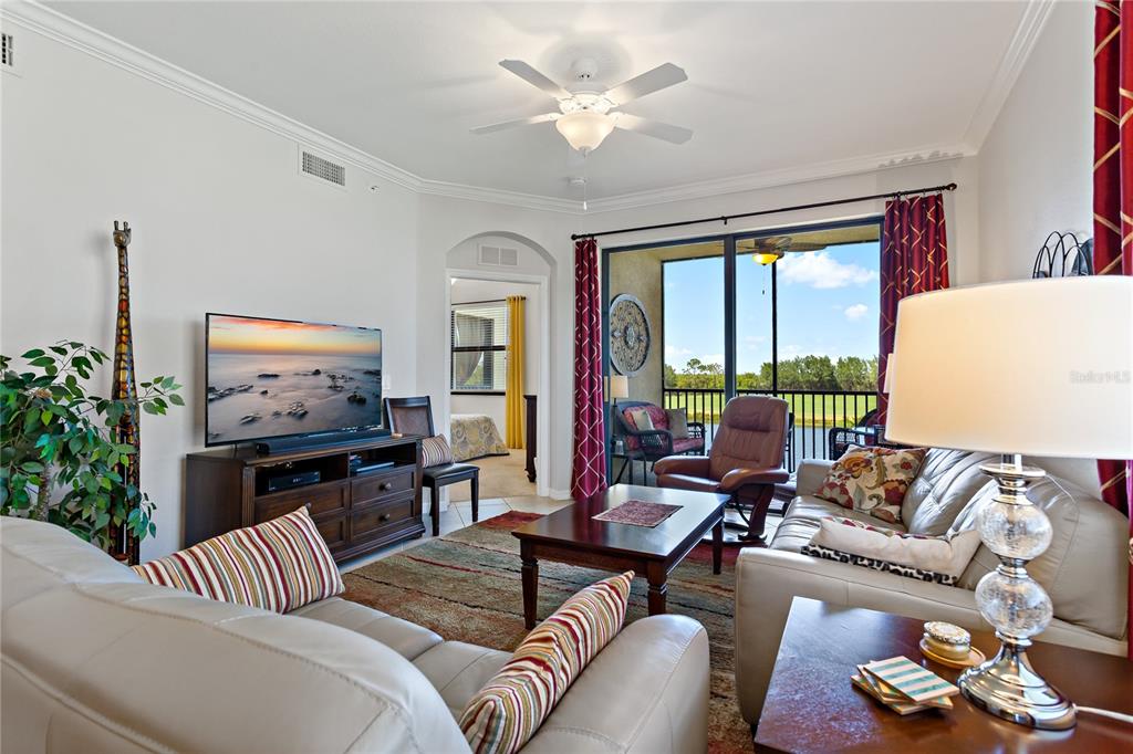 A living room features a leather sofa, a television, and a sliding door to a balcony — 7015 RIVER HAMMOCK DRIVE UNIT 208, BRADENTON, FL