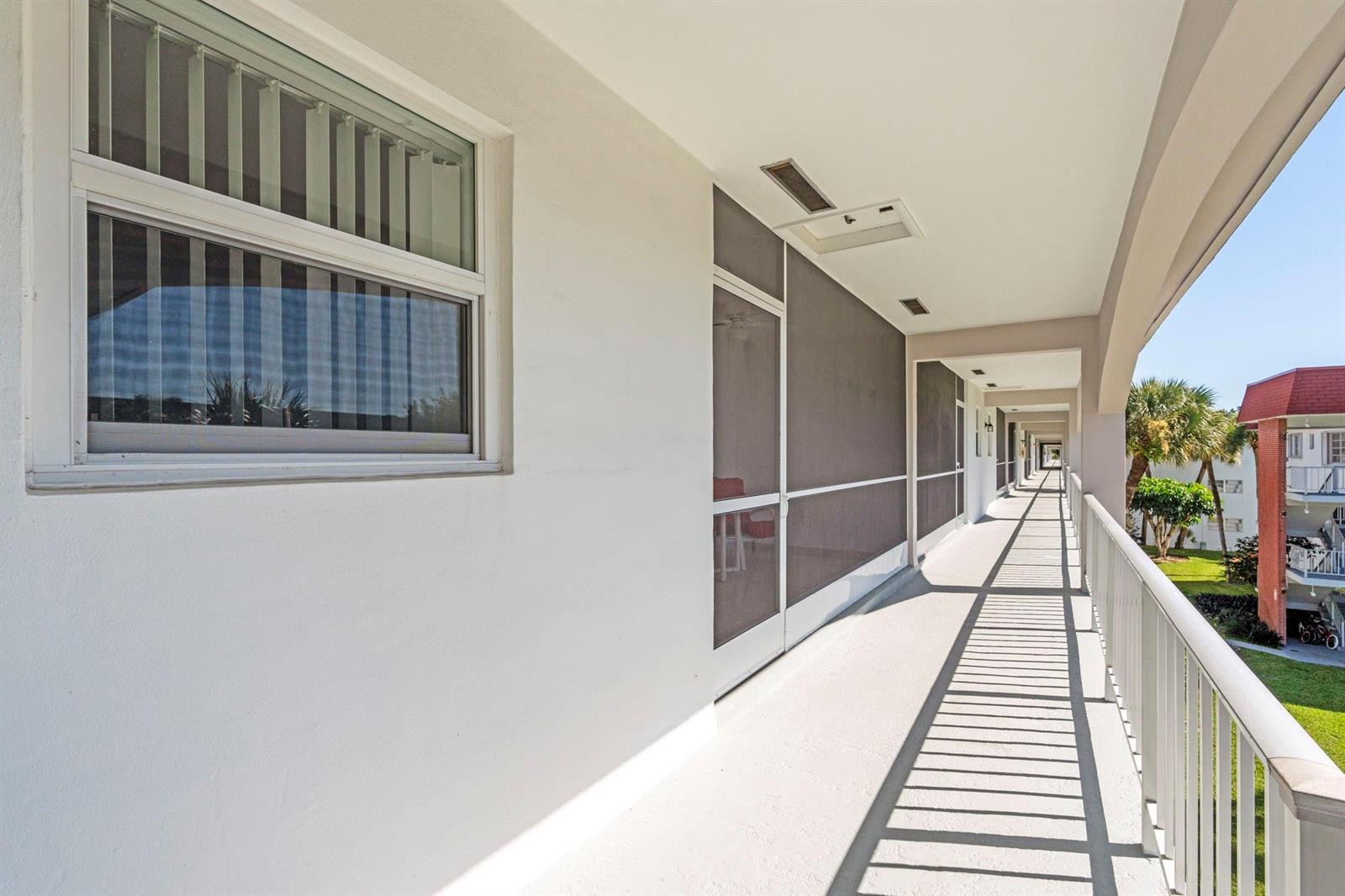 A long, covered outdoor walkway features white walls, screened enclosures, and a metal railing — 581 Blue Heron Drive # b, Hallandale Beach FL 33009, HALLANDALE BEACH, FL