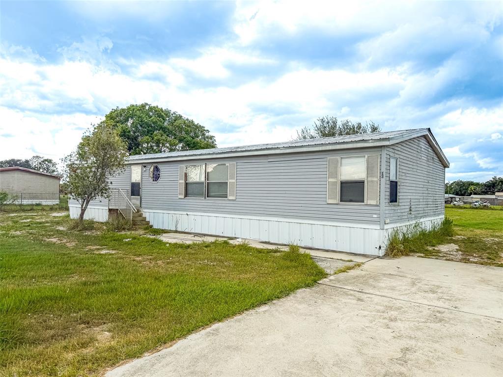 A single-story manufactured home with gray siding sits on a lot with a concrete driveway — 13 CACTUS CIRCLE E, WINTER HAVEN, FL