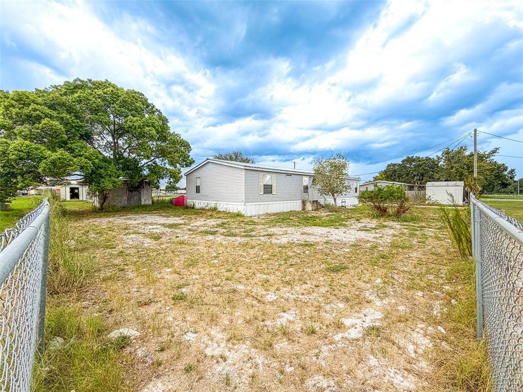 A manufactured home sits on a large, grassy lot with a chain-link fence — 13 CACTUS CIRCLE E, WINTER HAVEN, FL