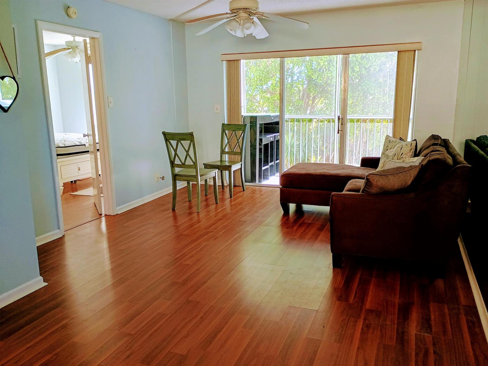 A living room with wood flooring, two green chairs, a brown sofa, and sliding doors — 1810 New Palm Way # 215, Boynton Beach FL 33435, BOYNTON BEACH, FL