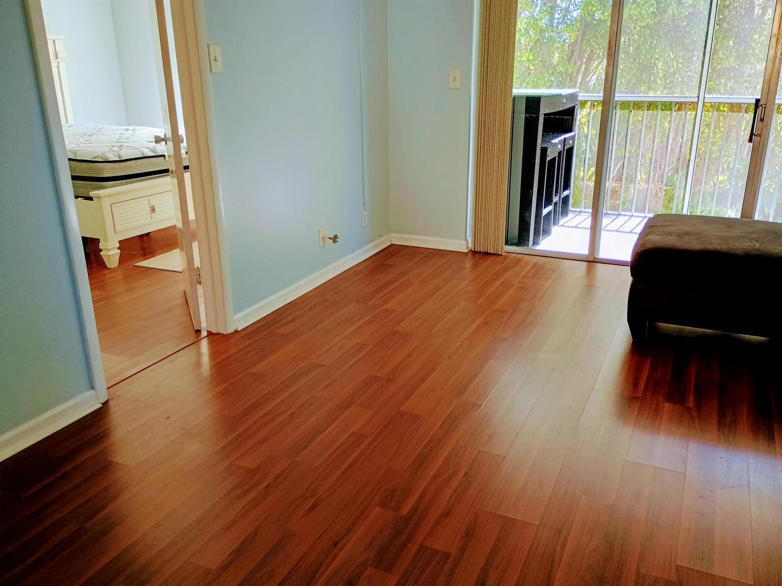 A room with wood-look flooring, light blue walls, and a sliding glass door to a balcony — 1810 New Palm Way # 215, Boynton Beach FL 33435, BOYNTON BEACH, FL