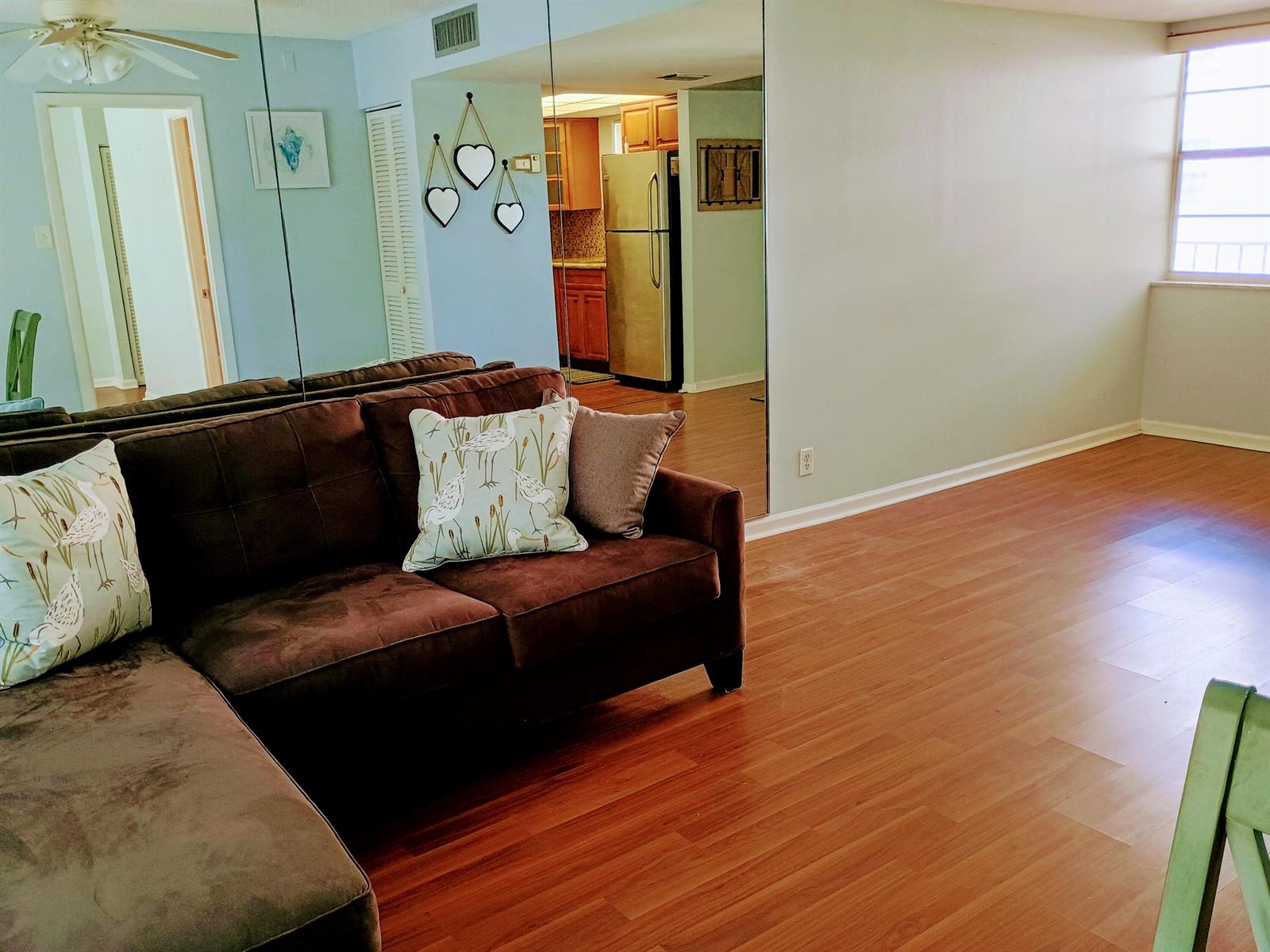 A living room with a brown sectional sofa, wood flooring, and a large mirrored wall — 1810 New Palm Way # 215, Boynton Beach FL 33435, BOYNTON BEACH, FL