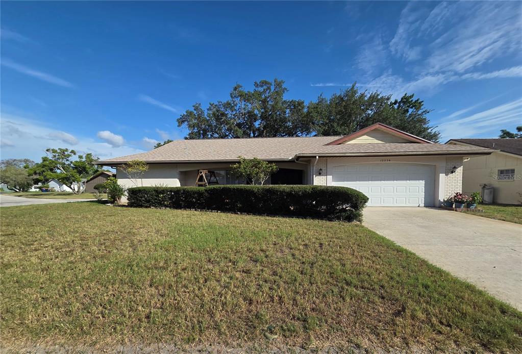 A single-story house with a beige exterior, a two-car garage, and a large front lawn — 12226 MEADOWBROOK LANE, HUDSON, FL