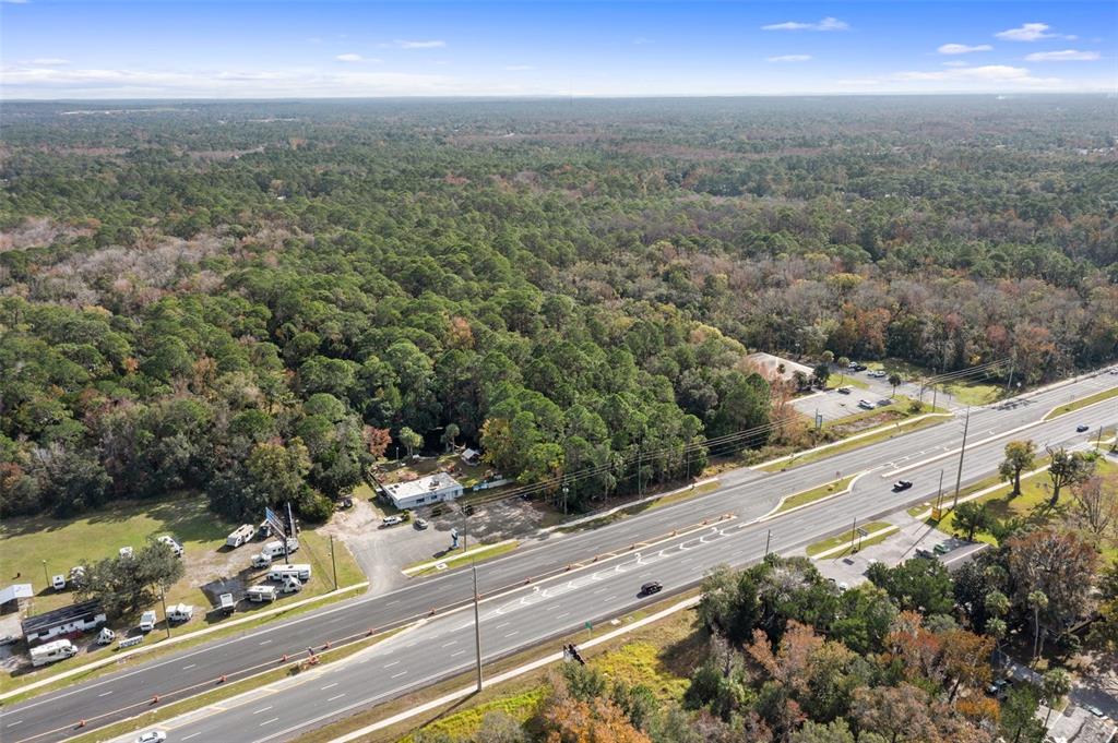 An aerial view shows a multi-lane highway bordering a wooded area with several small buildings — 3409 S SUNCOAST BOULEVARD, HOMOSASSA, FL