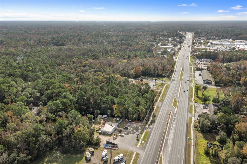 An aerial view shows a multi-lane highway running alongside a wooded area and a building — 3409 S SUNCOAST BOULEVARD, HOMOSASSA, FL