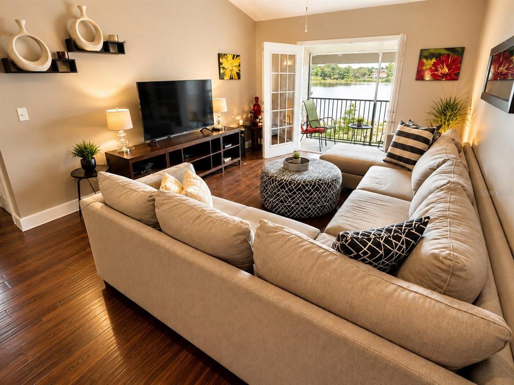 A living room features a large sectional sofa, a television, and a balcony overlooking water — 145 N PEARL LAKE CAUSEWAY UNIT 210, ALTAMONTE SPRINGS, FL