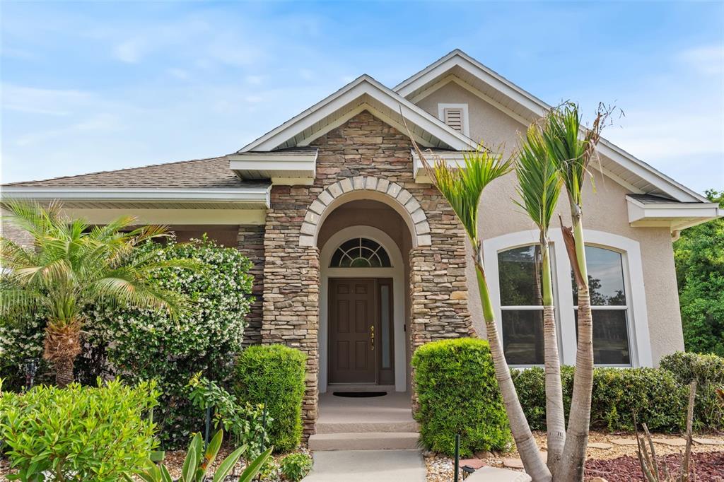 A single-story house exterior features a stone-accented arched entryway and a brown front door — 8434 WESTERLAND DRIVE, LAND O LAKES, FL