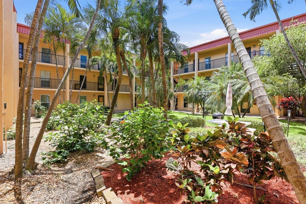 A courtyard with palm trees, landscaping, and a multi-story apartment building with balconies — 8911 BLIND PASS ROAD UNIT 103, ST PETE BEACH, FL