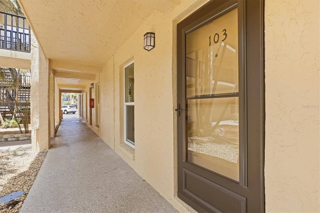 A view of an outdoor apartment walkway with a brown door labeled 103 — 8911 BLIND PASS ROAD UNIT 103, ST PETE BEACH, FL