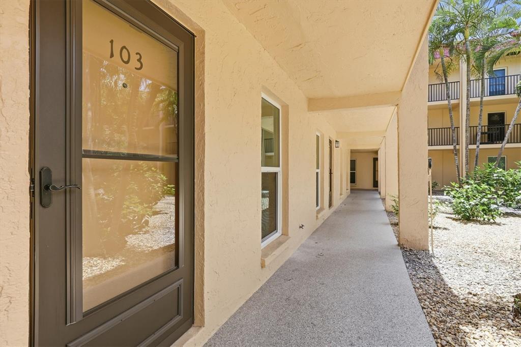 A ground-level apartment entrance with a screen door labeled 103 along a concrete walkway — 8911 BLIND PASS ROAD UNIT 103, ST PETE BEACH, FL