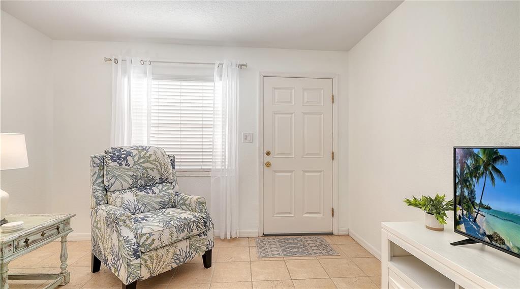 A living room features a patterned armchair, a white door, and a television on a stand — 1749 HILLVIEW STREET UNIT 1, SARASOTA, FL