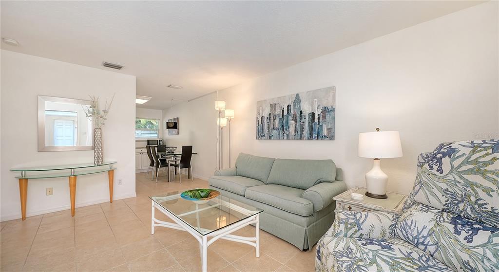 A living room with a light green sofa, glass coffee table, and a dining area beyond — 1749 HILLVIEW STREET UNIT 1, SARASOTA, FL